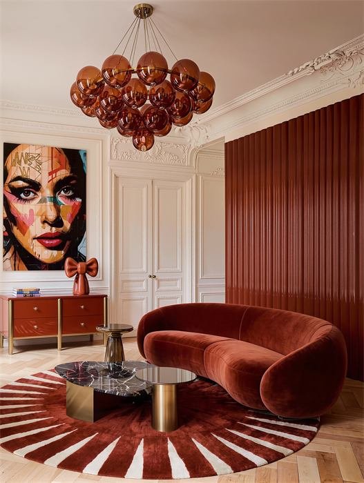 Salon avec canapé en velours rouge, tapis rayonnant et lustre ambré – projet L'Azur, Cannes
