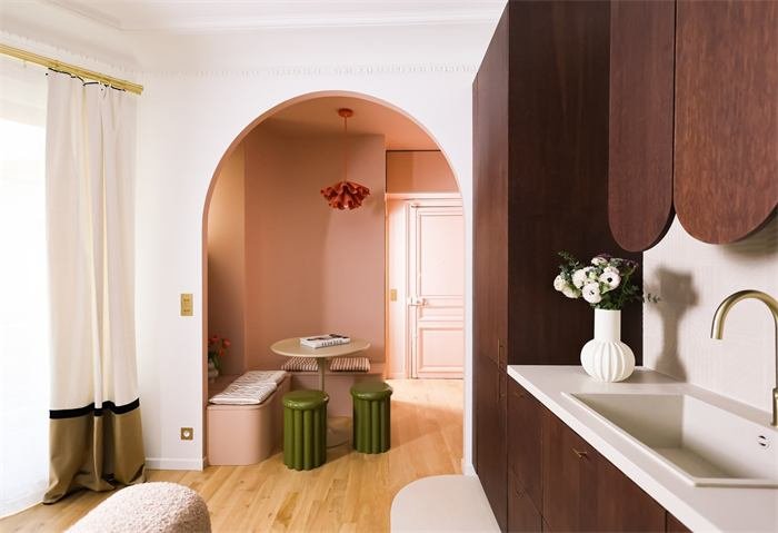 Coin repas rose sous une arche et cuisine en bois foncé – projet Le Cyprès, Paris